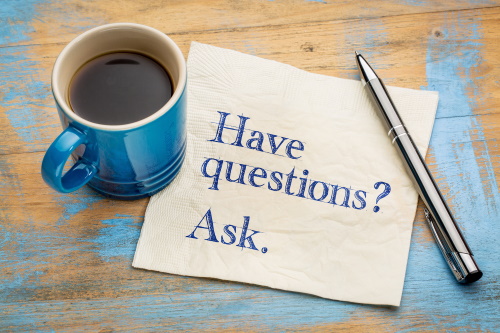 A picture of a table with a mug of coffee, a pen, and a piece of paper that reads "Have questions? Ask.".