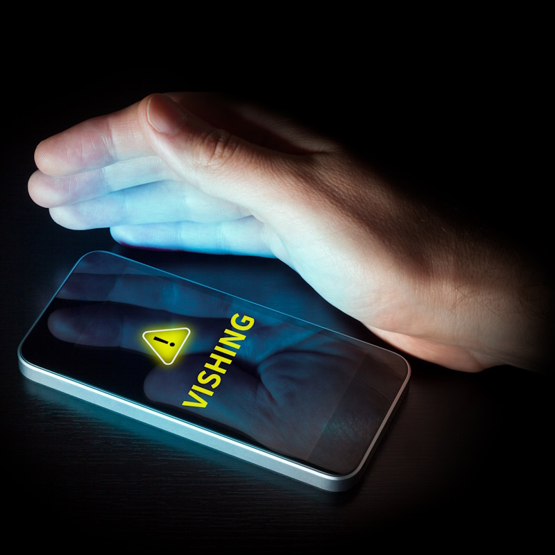 An image of a hand hovering over a dimly lit cell phone screen that reads "Vishing".