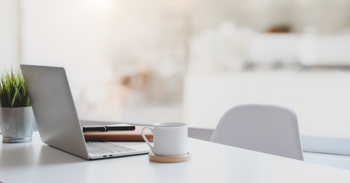An image of a laptop, coffee mug, and fake plant sitting on a desk.