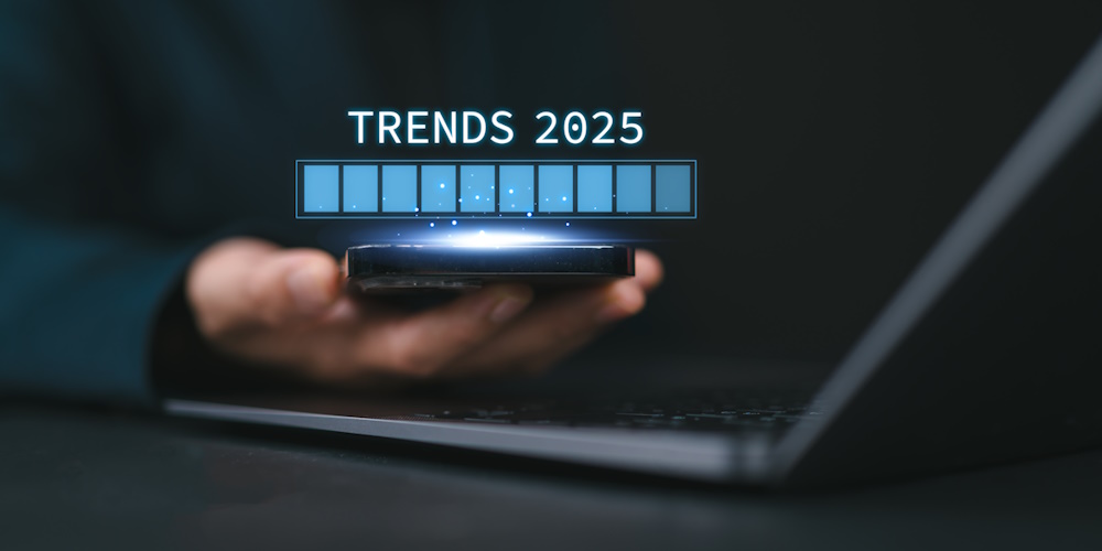 An image of a man hold his phone just above his laptop. Above the phone is a full gauge and above the gauge it reads "Trends 2025"