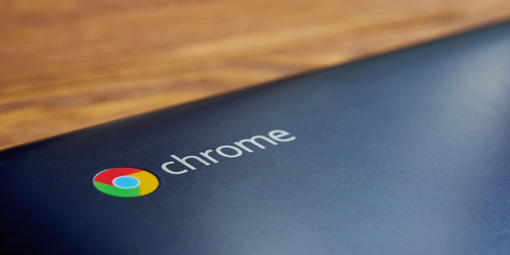 Black laptop that is Chrome based showing the Chrome Logo, on a wood background.