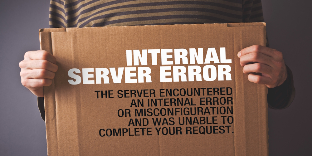 A person in a striped shirt holds a cardboard sign with the message "INTERNAL SERVER ERROR. The server encountered an internal error or misconfiguration and was unable to complete your request."