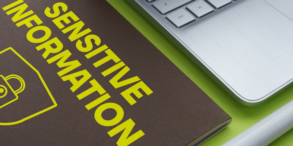 An image of a book laying next to a laptop that reads "sensitive information"