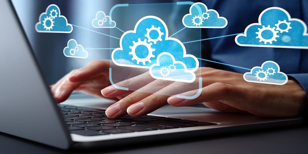 Hands typing on a laptop with digital cloud icons and gears representing cloud computing, automation, and data integration.